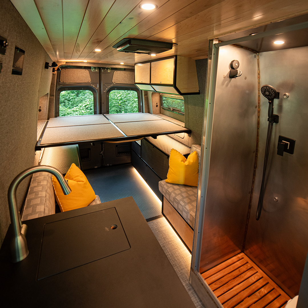 Compact living space with a bed, seating area, and shower in a small room.